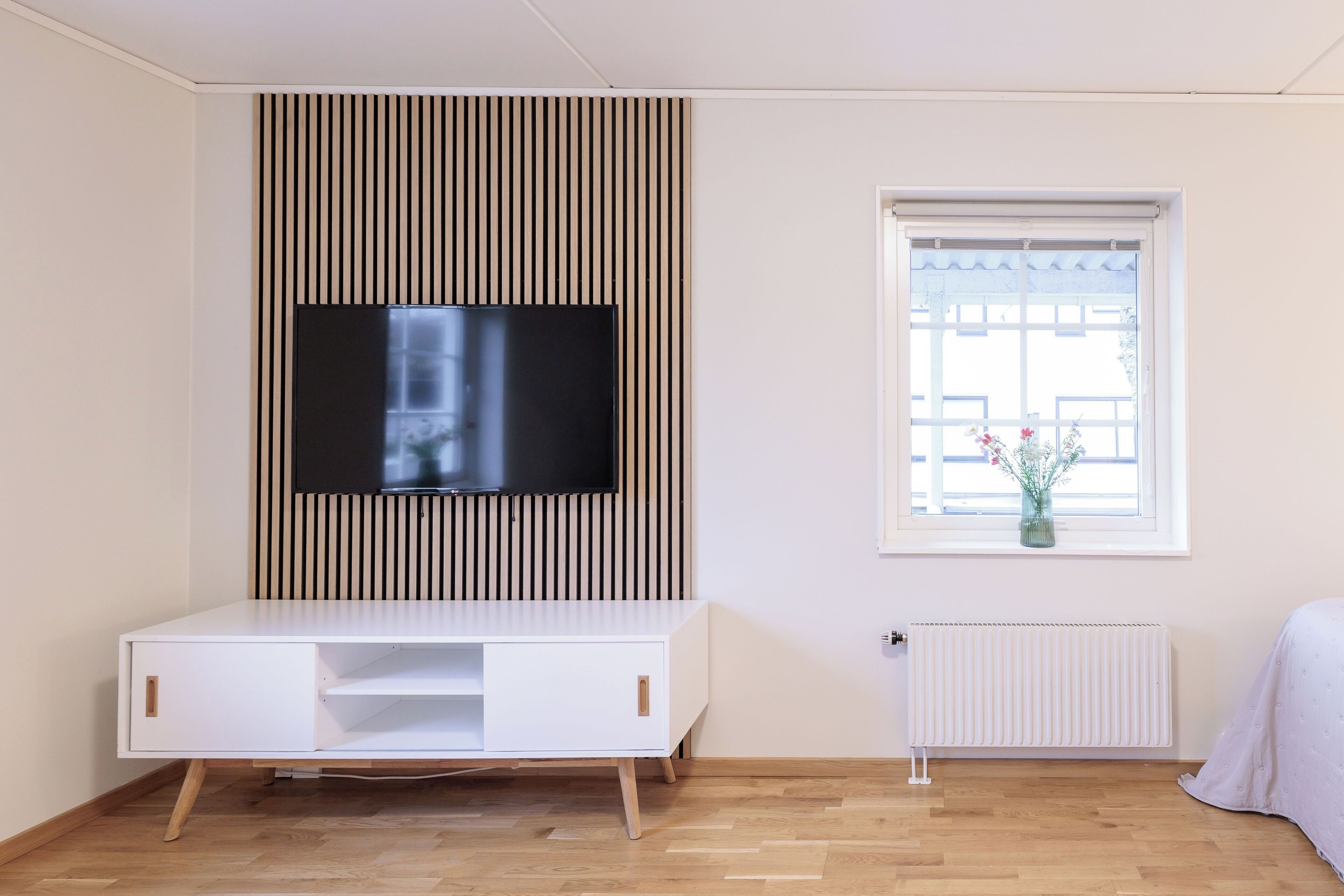 Een moderne kamer met een witte tv-meubel, een wandtelevisie, een raam met uitzicht en een radiator.