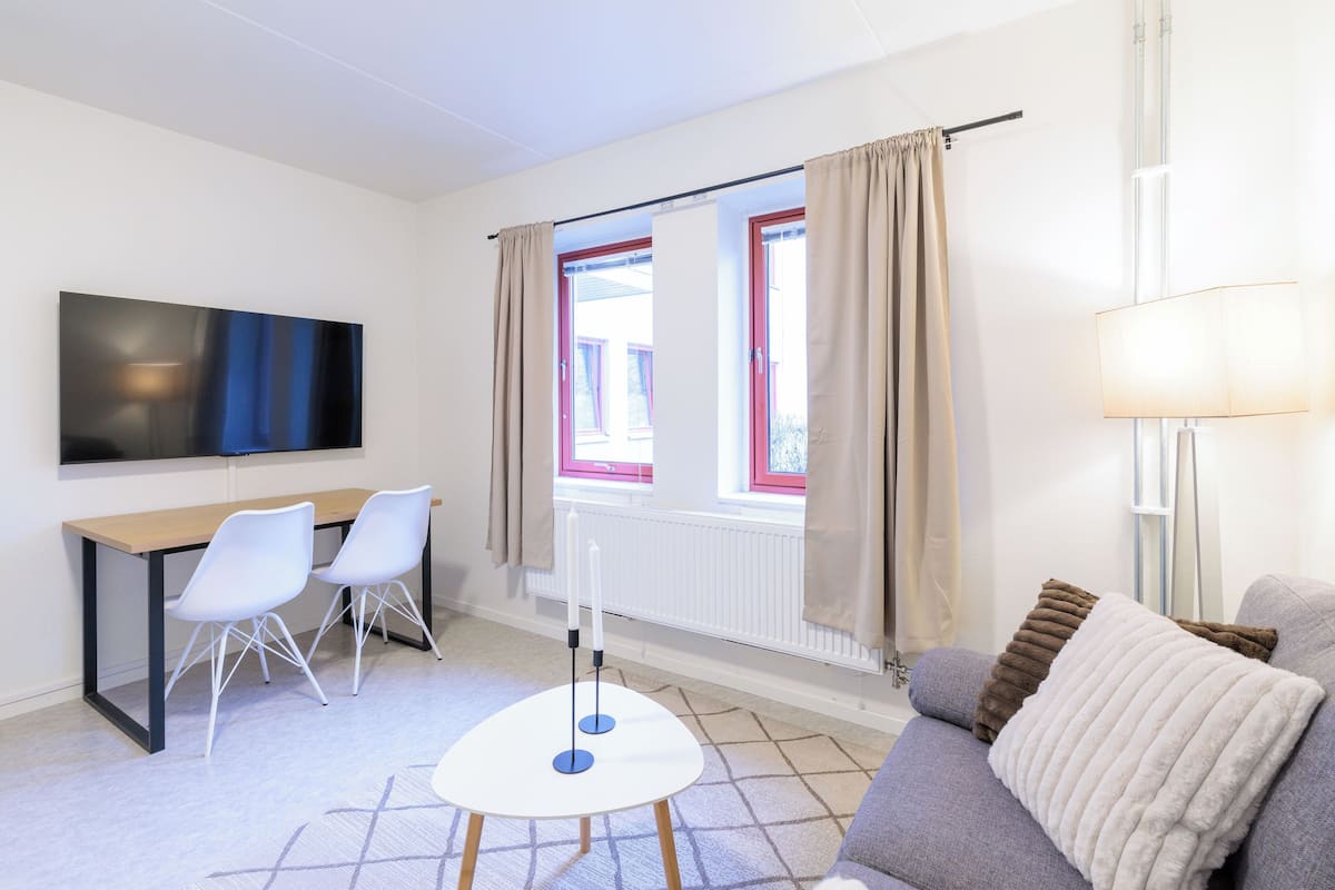 Ein modernes Zimmer mit Fernseher, einem Esstisch mit Stühlen, einer Couch und einer Lampe.