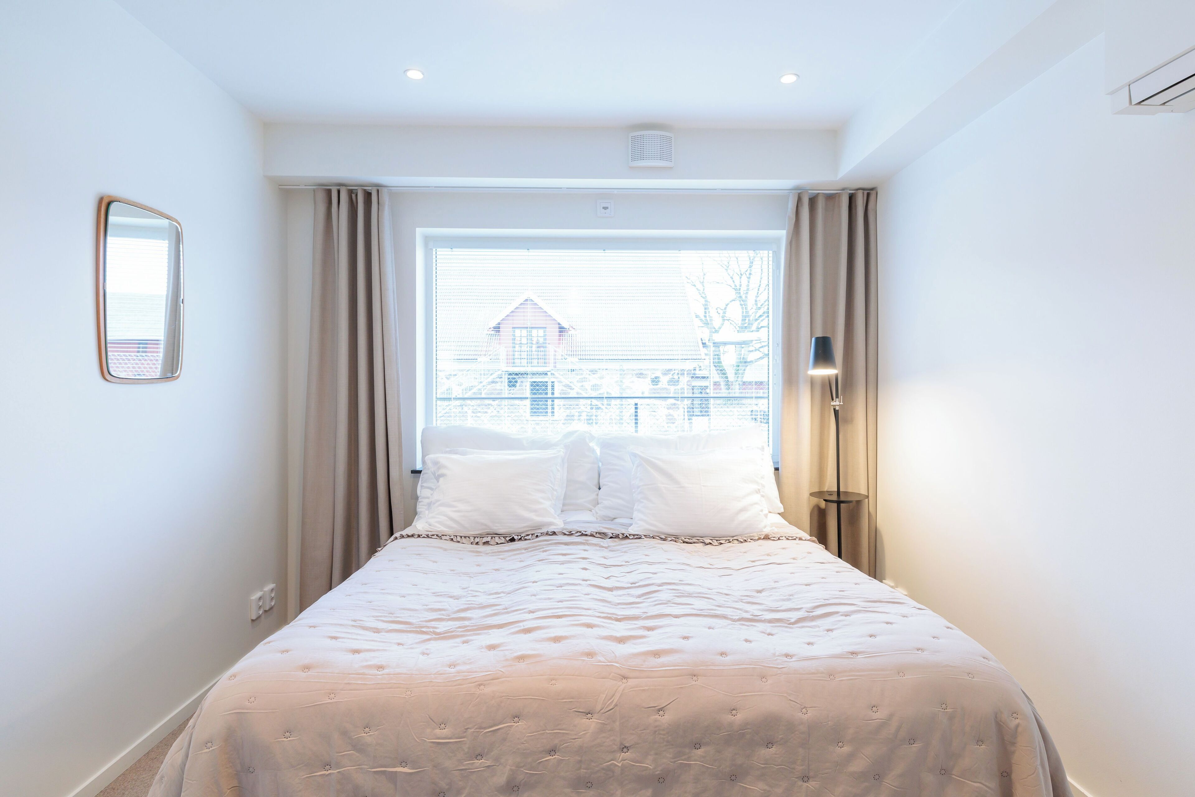 Un lit bien fait, recouvert d’une couvre-lit à motifs, une lampe de chevet et une fenêtre avec des rideaux.
