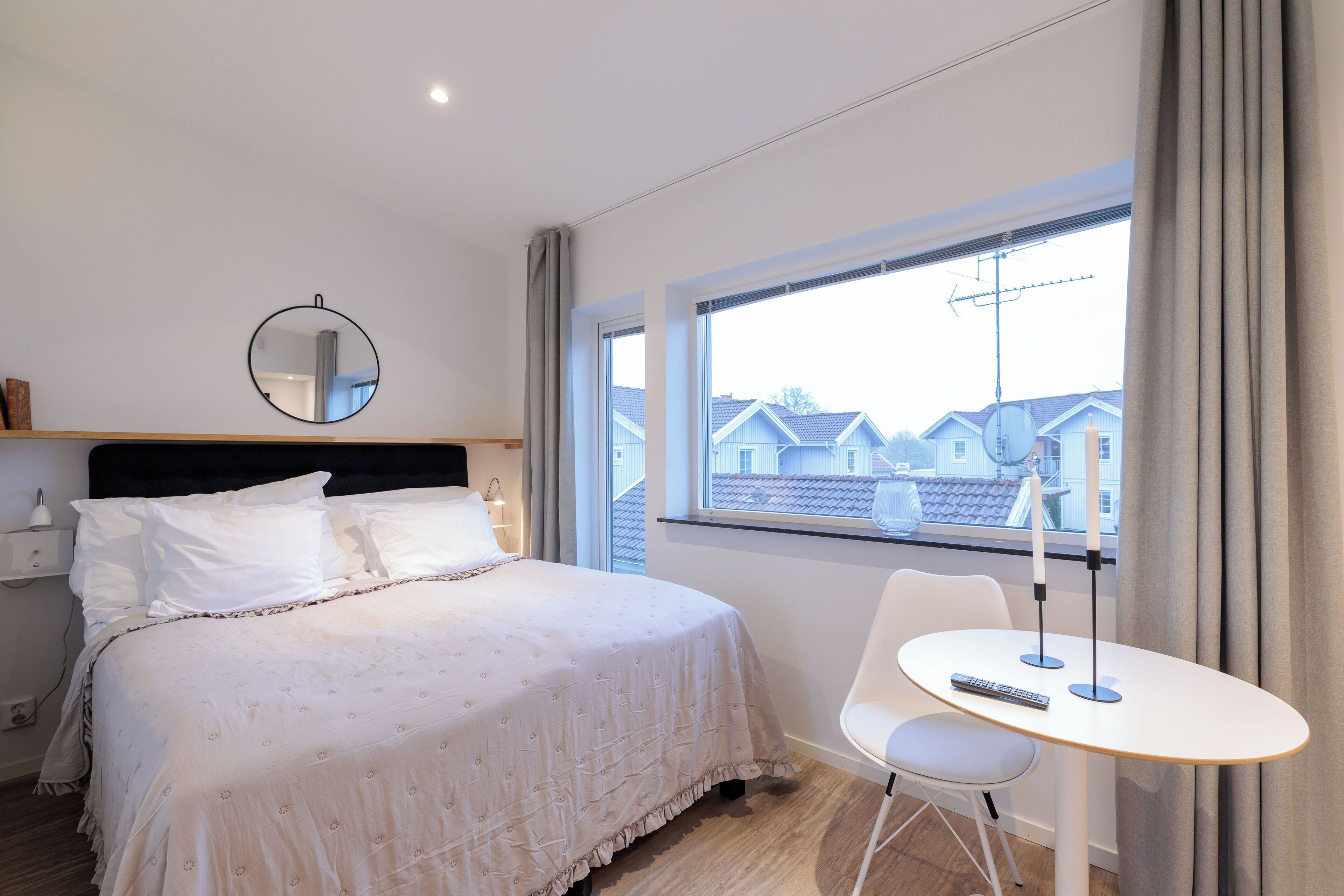 A neatly made bed with a headboard, a bedside table with a remote control, and a window with curtains.