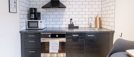 Una cocina pequeña equipada con microondas, cafetera y una campana extractora negra.