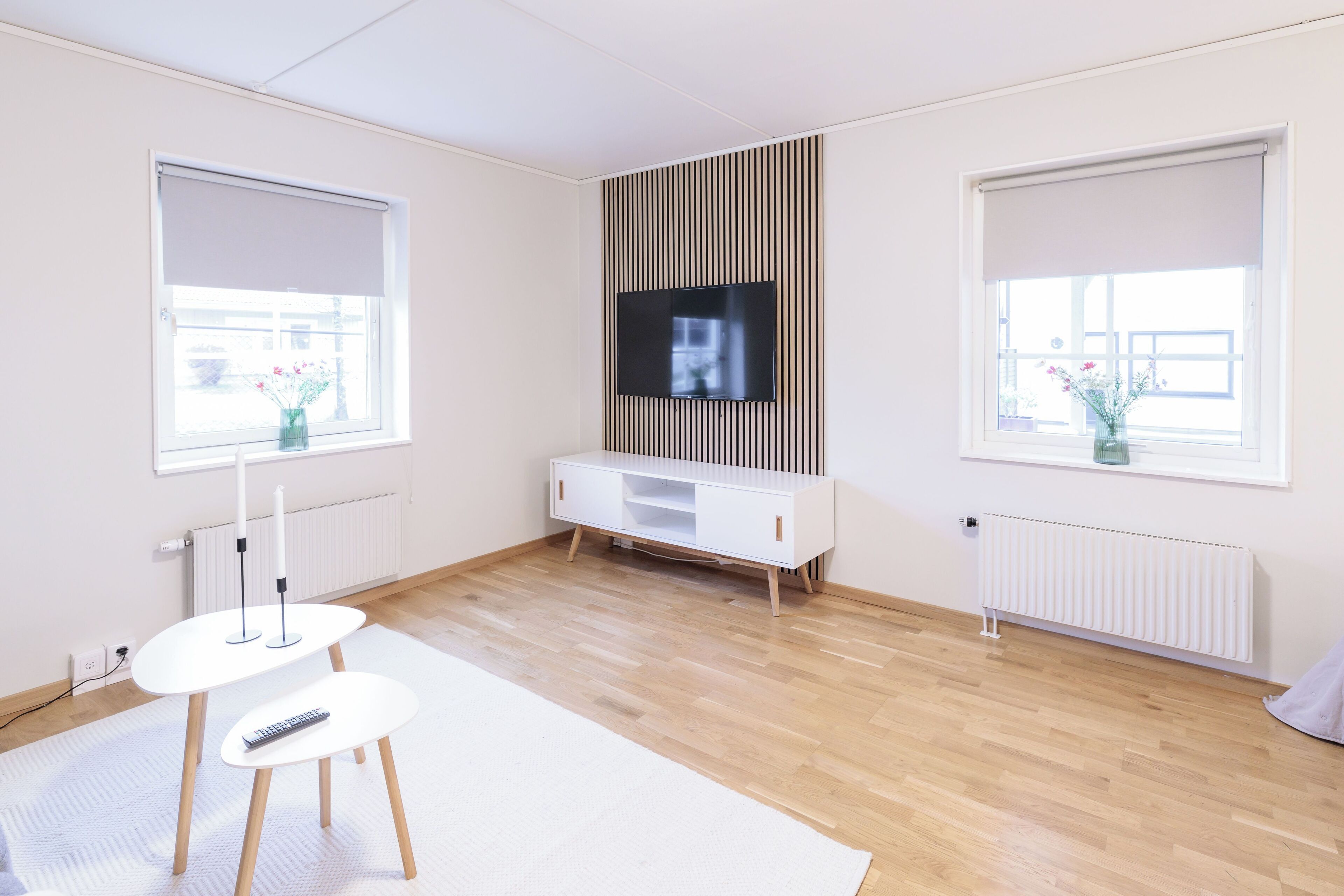 Habitació moderna amb televisió de pantalla plana penjada a la paret, un armari blanc i una taula petita amb un comandament a distància.