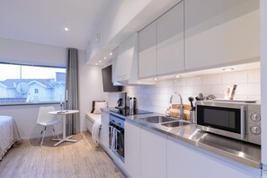 Eine moderne Küche mit Edelstahlgeräten, ein Essbereich mit einem weißen Tisch und Stuhl und ein Fenster mit Blick auf Häuser.