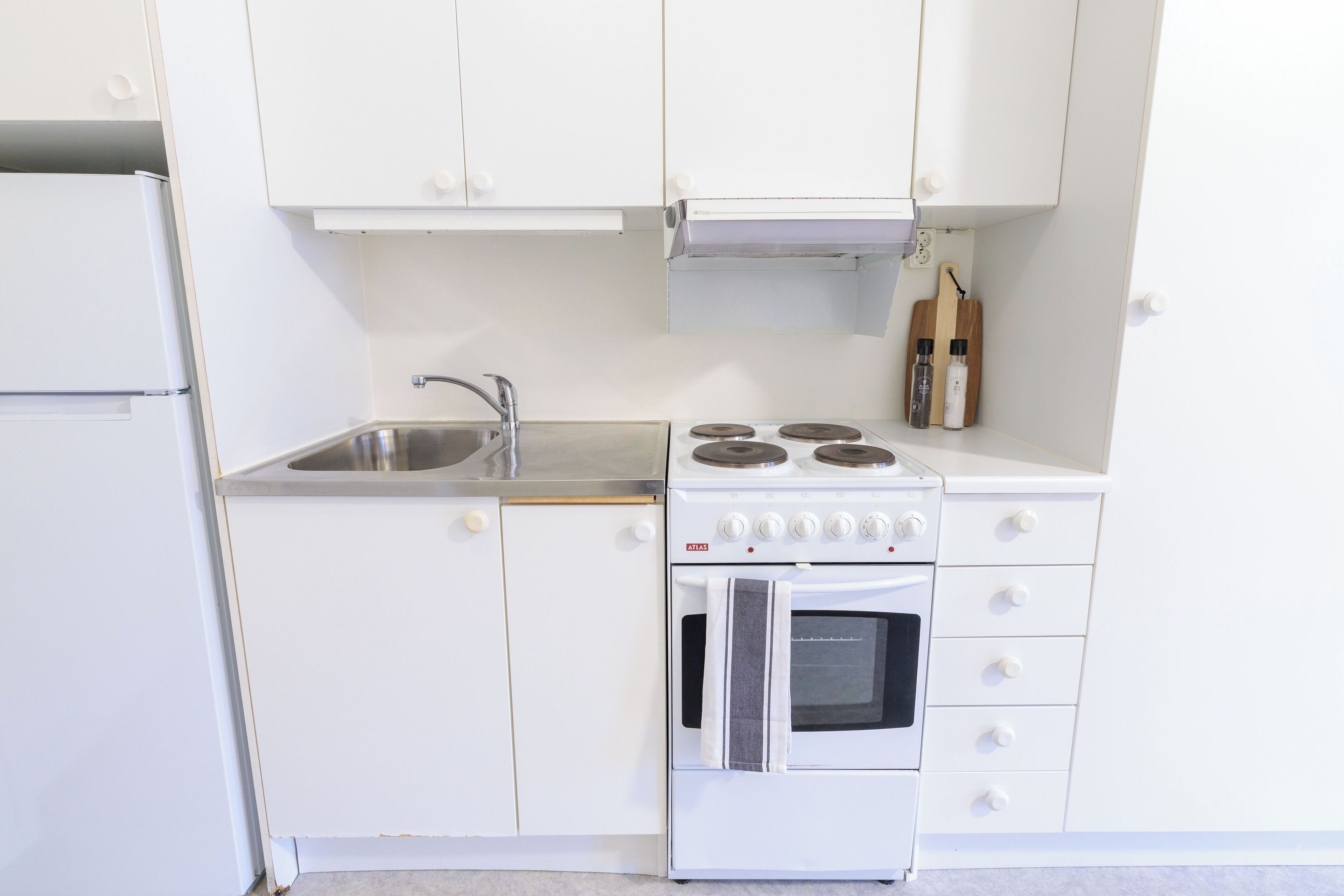 Una cucina compatta con mobili bianchi, un lavello in acciaio inossidabile, un fornello e un forno.