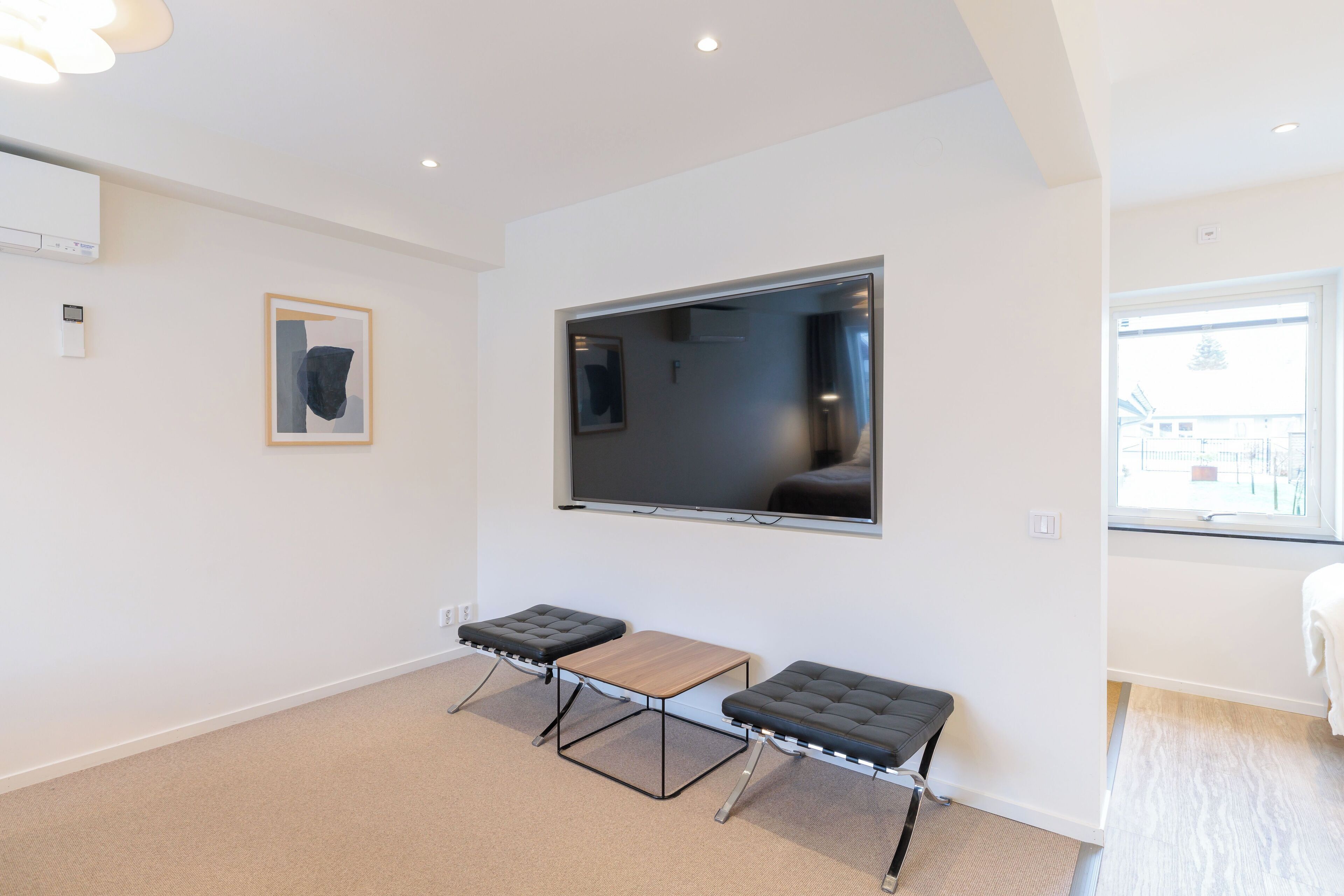 Uma sala de estar moderna com uma TV de tela plana na parede, duas áreas de estar acolchoadas em preto e uma mesa de centro de madeira.