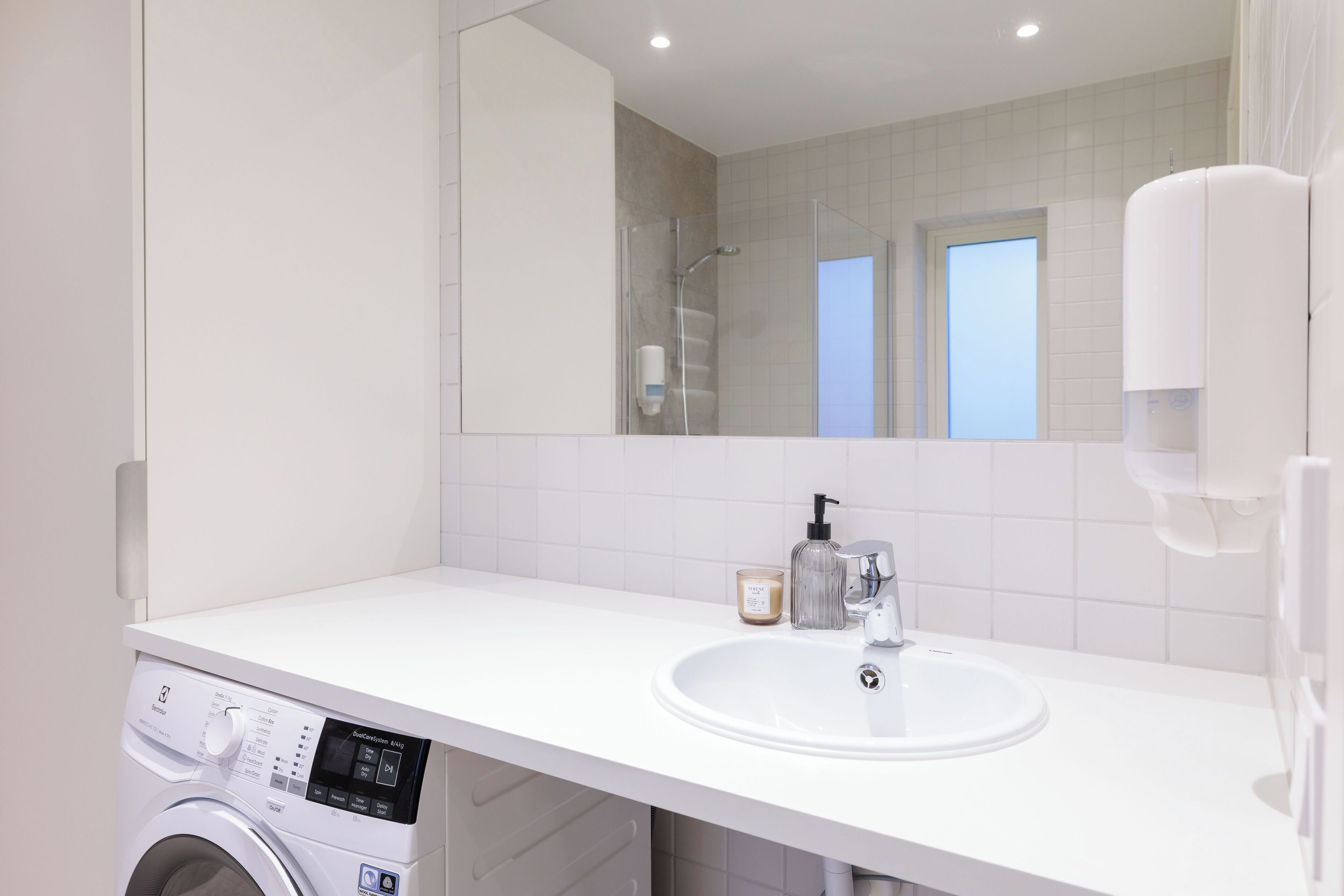A modern bathroom with a white sink, a glass shower enclosure, and a washing machine.