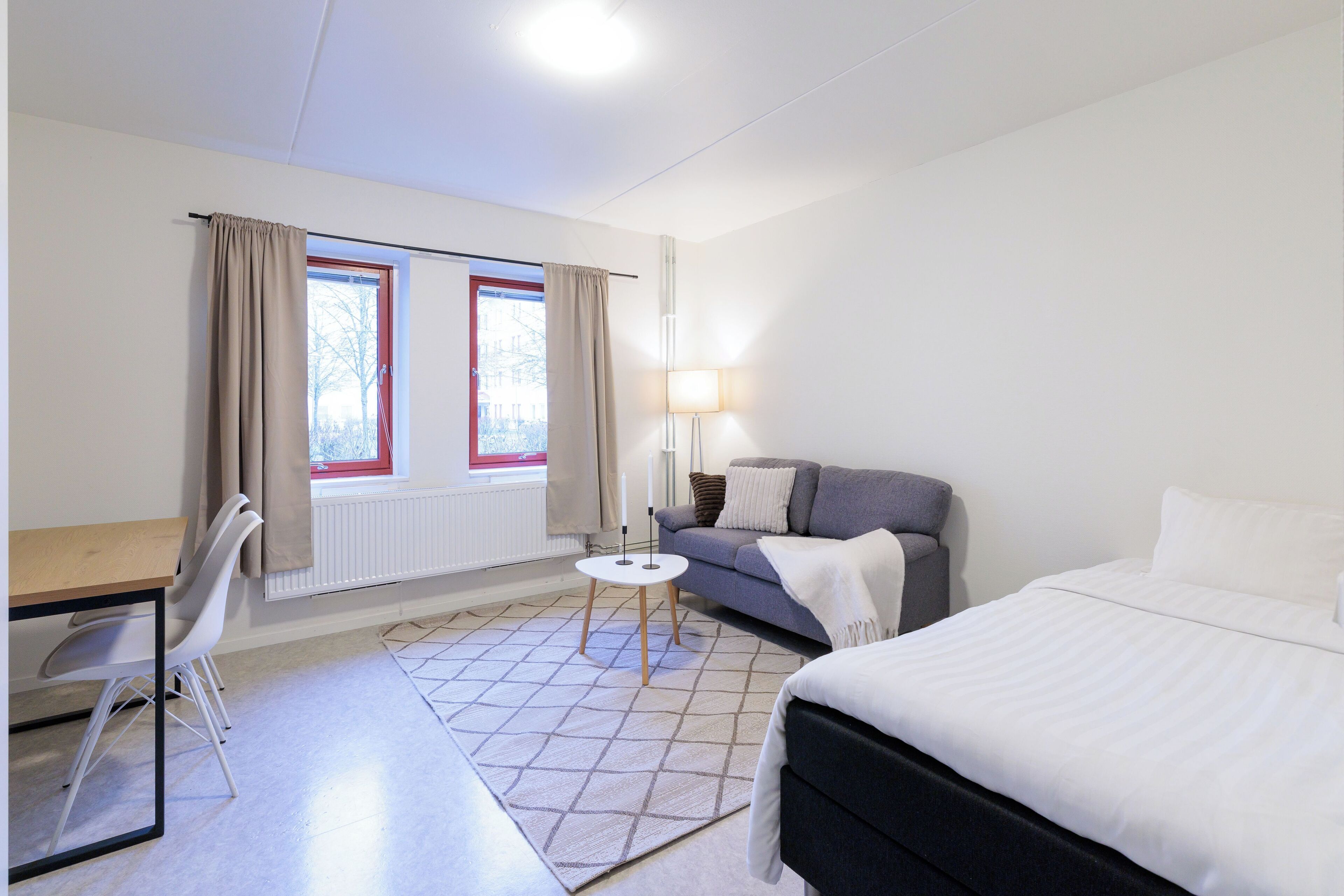 A hotel room with a bed, a desk with a chair, a sofa, a small round table, and a lamp.