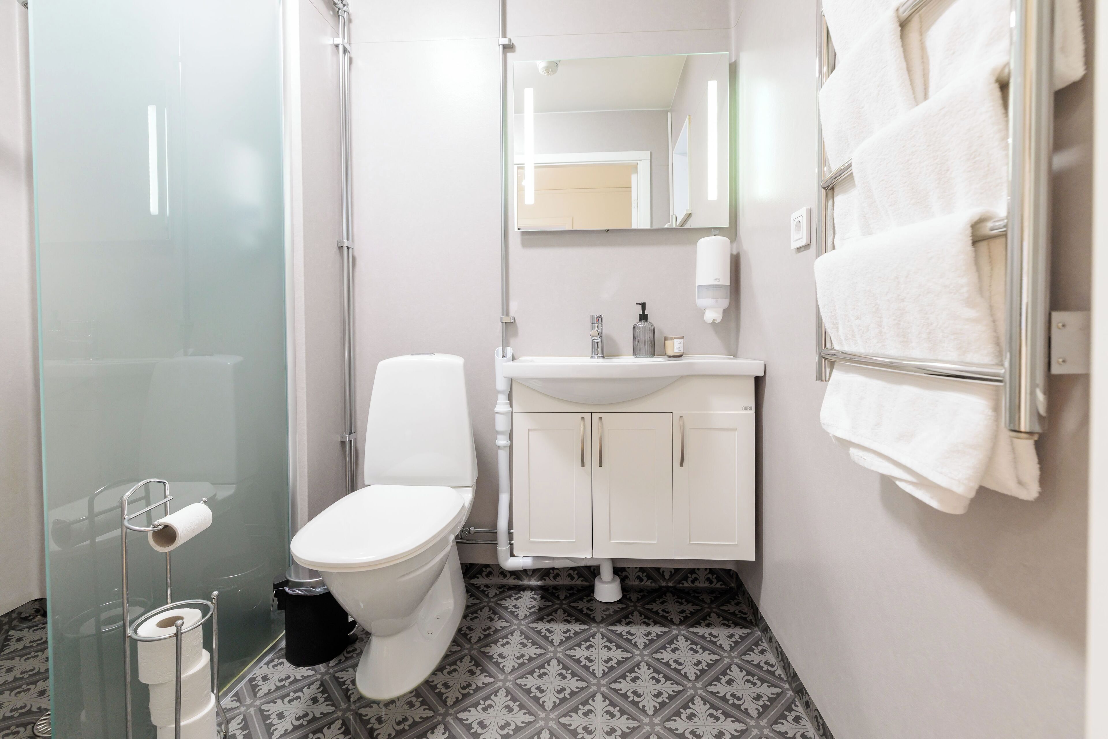 A bathroom with a glass shower enclosure, a toilet, a sink with a mirror above it, and a towel rack with towels.