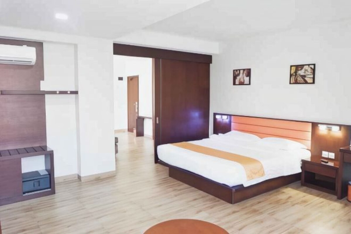 Une chambre d’hôtel moderne avec un grand lit, une tête de lit en bois, des tables de chevet et des œuvres d’art accrochées aux murs.