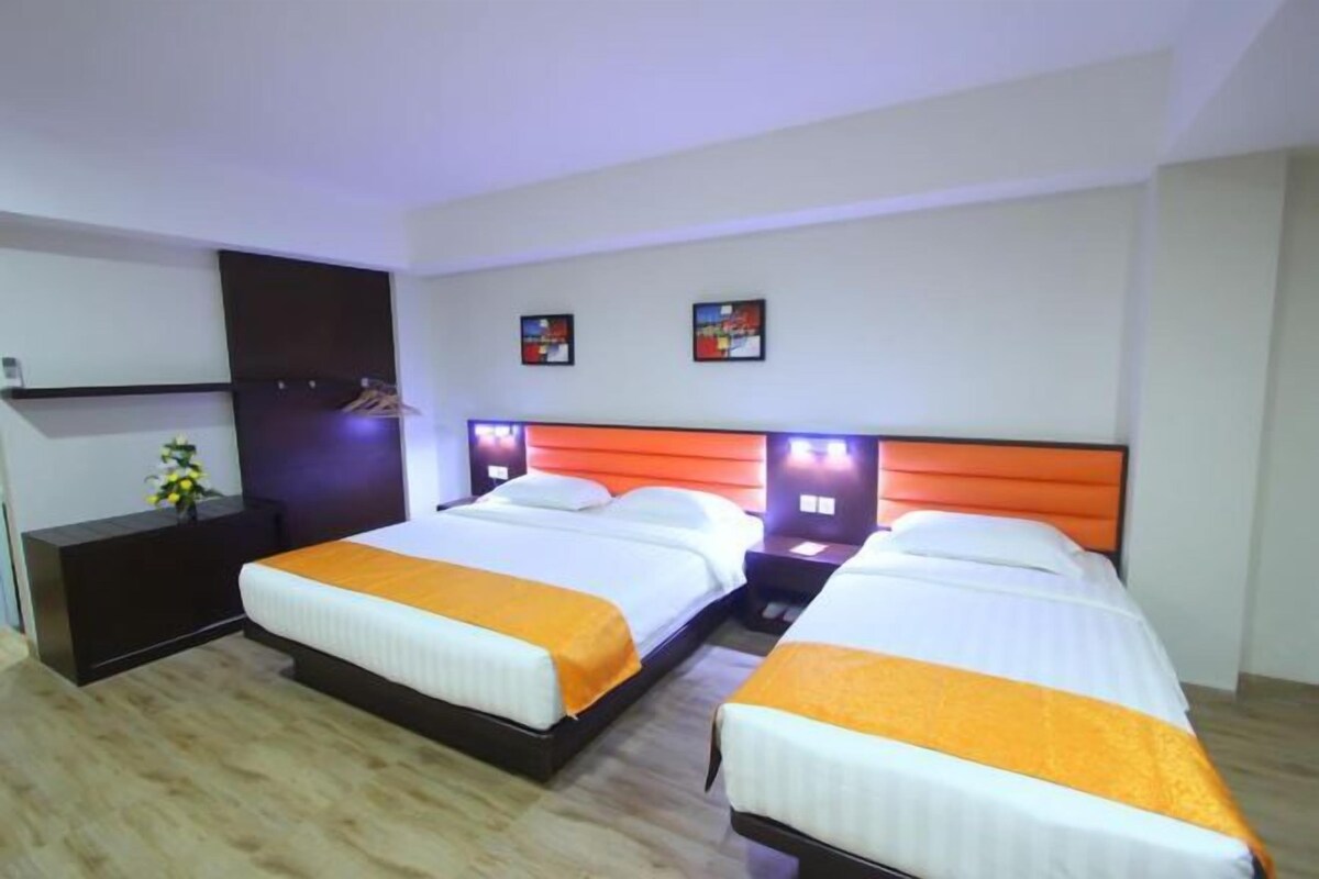 A hotel room with two beds, a dark wooden dresser, and a small table with a vase of flowers.