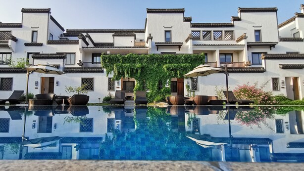 A pool reflecting a building with traditional architecture, including multiple balconies and a clear sky. - Huangshan Huizhou Creek Villa (Huangshan)