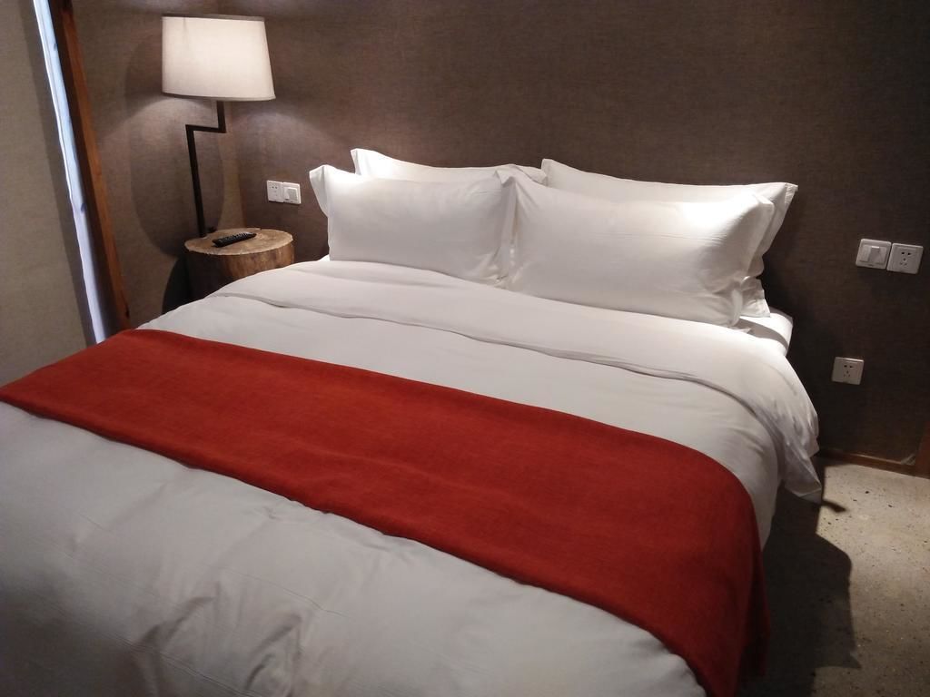 Una habitación de hotel con una cama, una manta roja, una lámpara y una mesita de noche de madera.