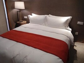 Una habitación de hotel con una cama, una manta roja, una lámpara y una mesita de noche de madera.