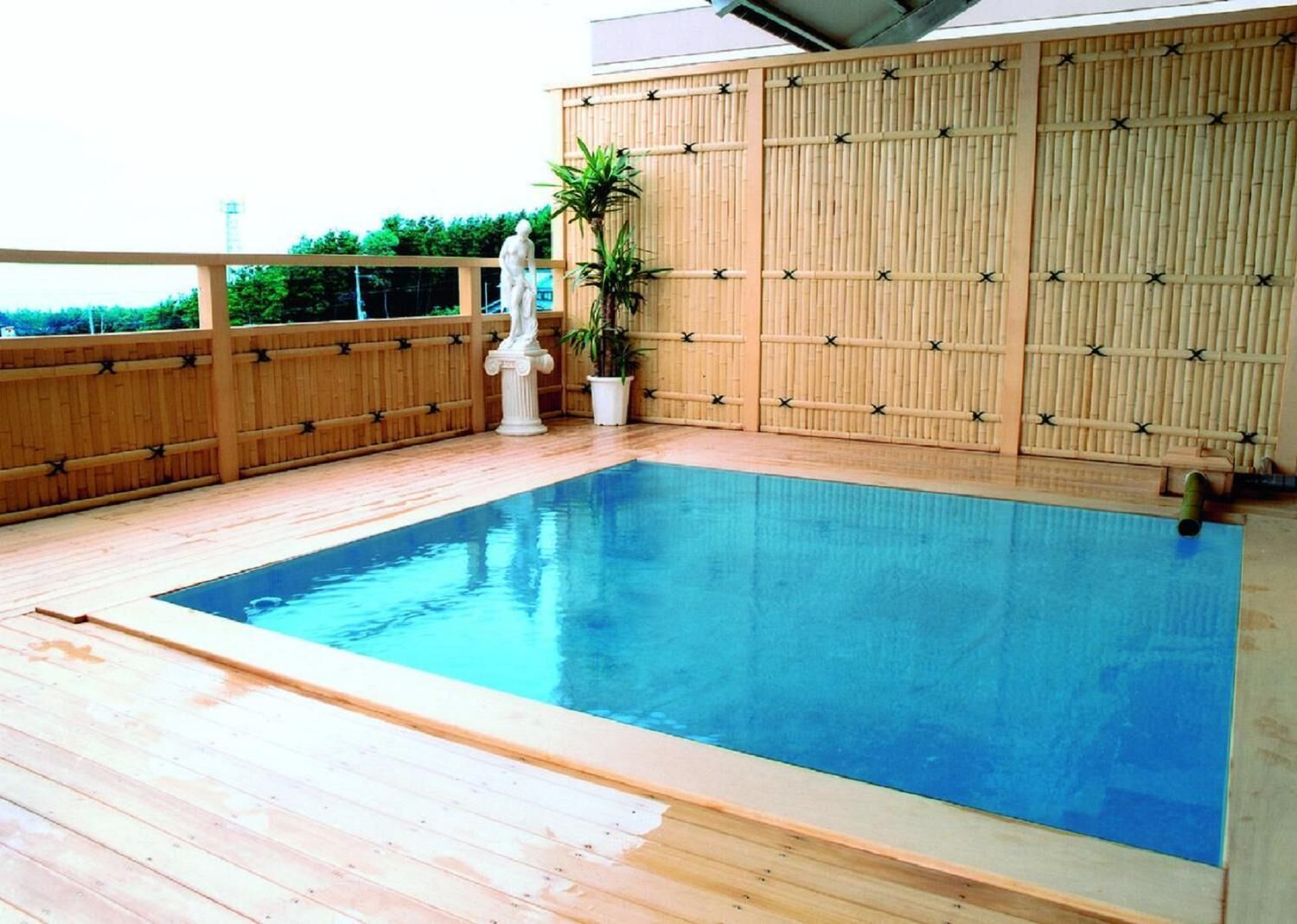 A swimming pool with a wooden deck and a bamboo fence.