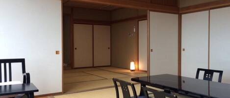 A traditional Japanese room with tatami flooring, a low table, and chairs with cushions.