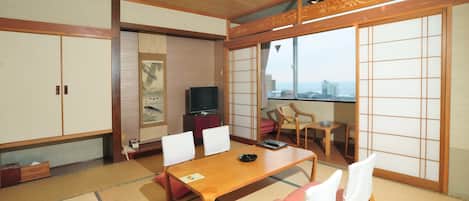 Una habitación tradicional japonesa con suelo de tatami, una mesa de madera, sillas, un televisor y puertas correderas.