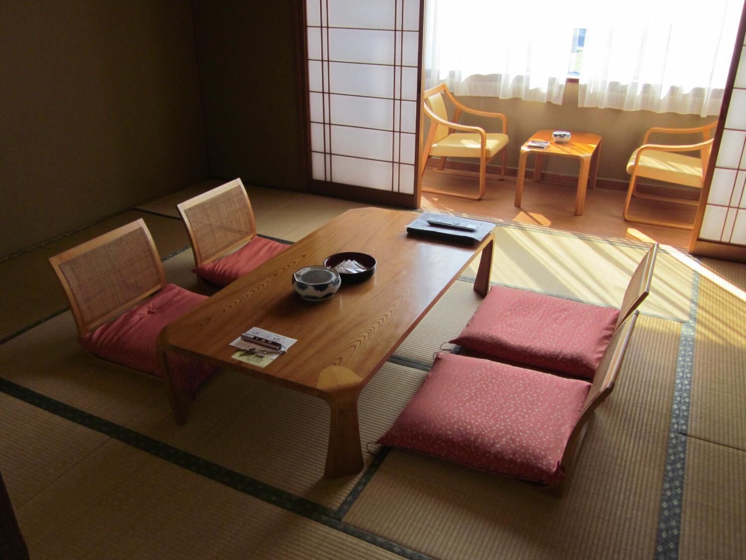 Ein traditioneller japanischer Raum mit Tatami-Böden, einem niedrigen Holztisch und einer Couch mit Kissen.