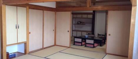 Une pièce de style japonais traditionnel, avec un sol recouvert de tatamis, des portes coulissantes et une petite table entourée de chaises.