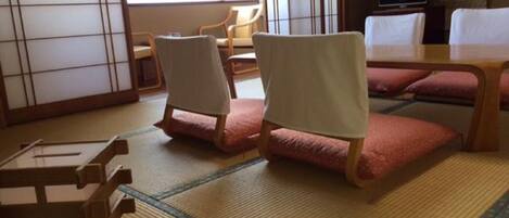 A traditional Japanese room with tatami flooring, a low wooden table, two chairs, a television, and a sliding door.