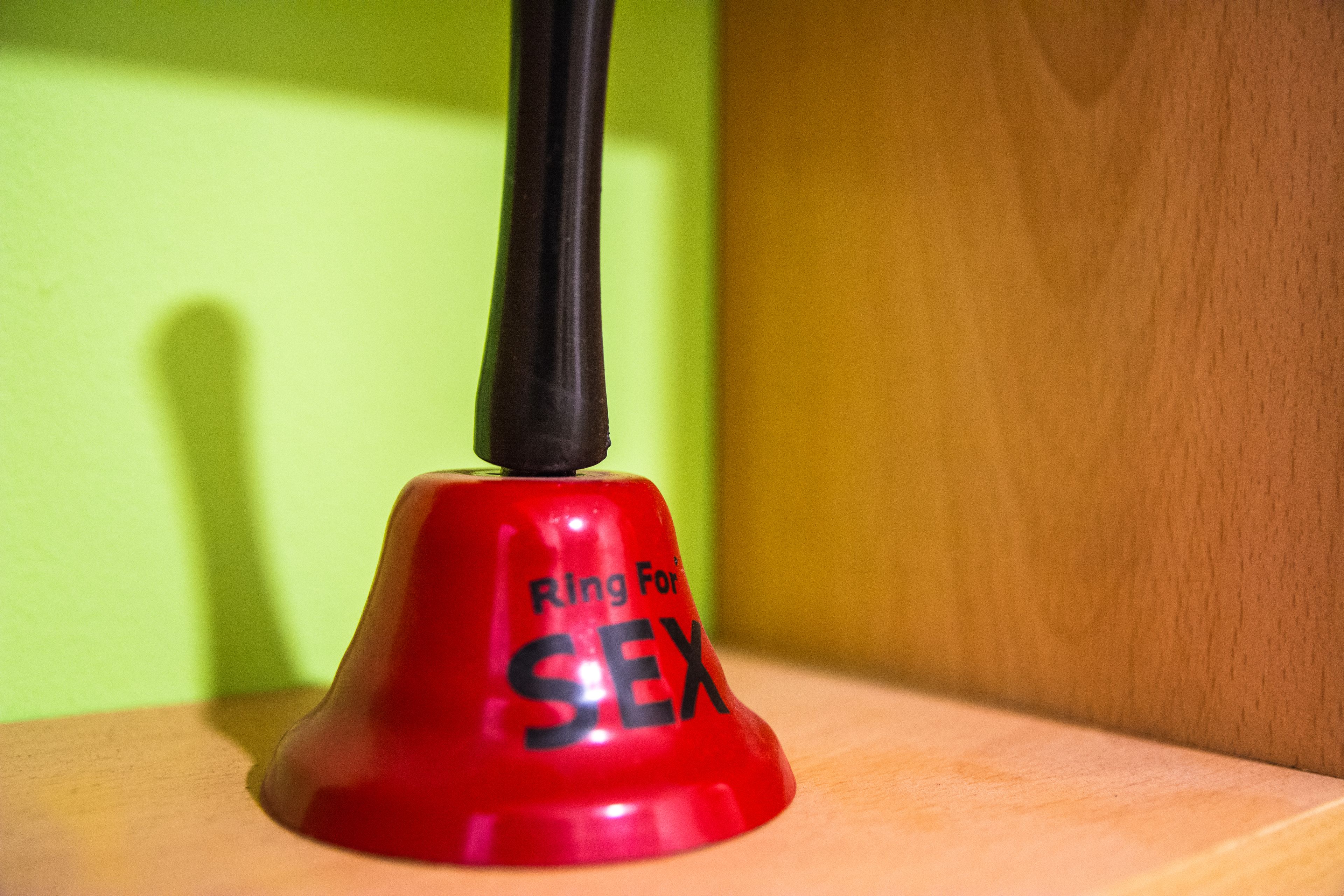 A red object with the text "Ring For SEX" on a wooden surface against a green background.