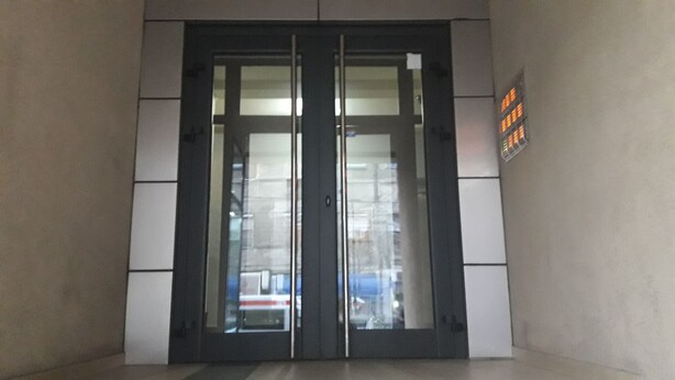 Unas puertas dobles con un panel de vidrio, un cartel a la derecha y el reflejo de un edificio en el vidrio.