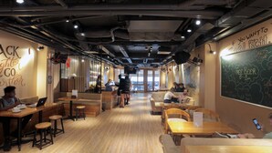 Un café avec des tables et des tabourets en bois, un menu écrit à la craie et une pancarte indiquant : « Si vous voulez partir, allez tout droit. »