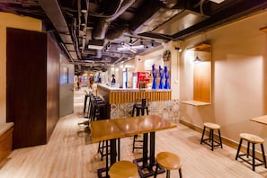 Un restaurante con una larga mesa de madera, taburetes de bar y una barra con refrigerador de Coca-Cola.