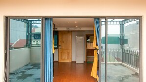 Une pièce dotée d’une porte-fenêtre coulissante donnant sur un balcon, d’une porte en bois et d’un petit coin cuisine.