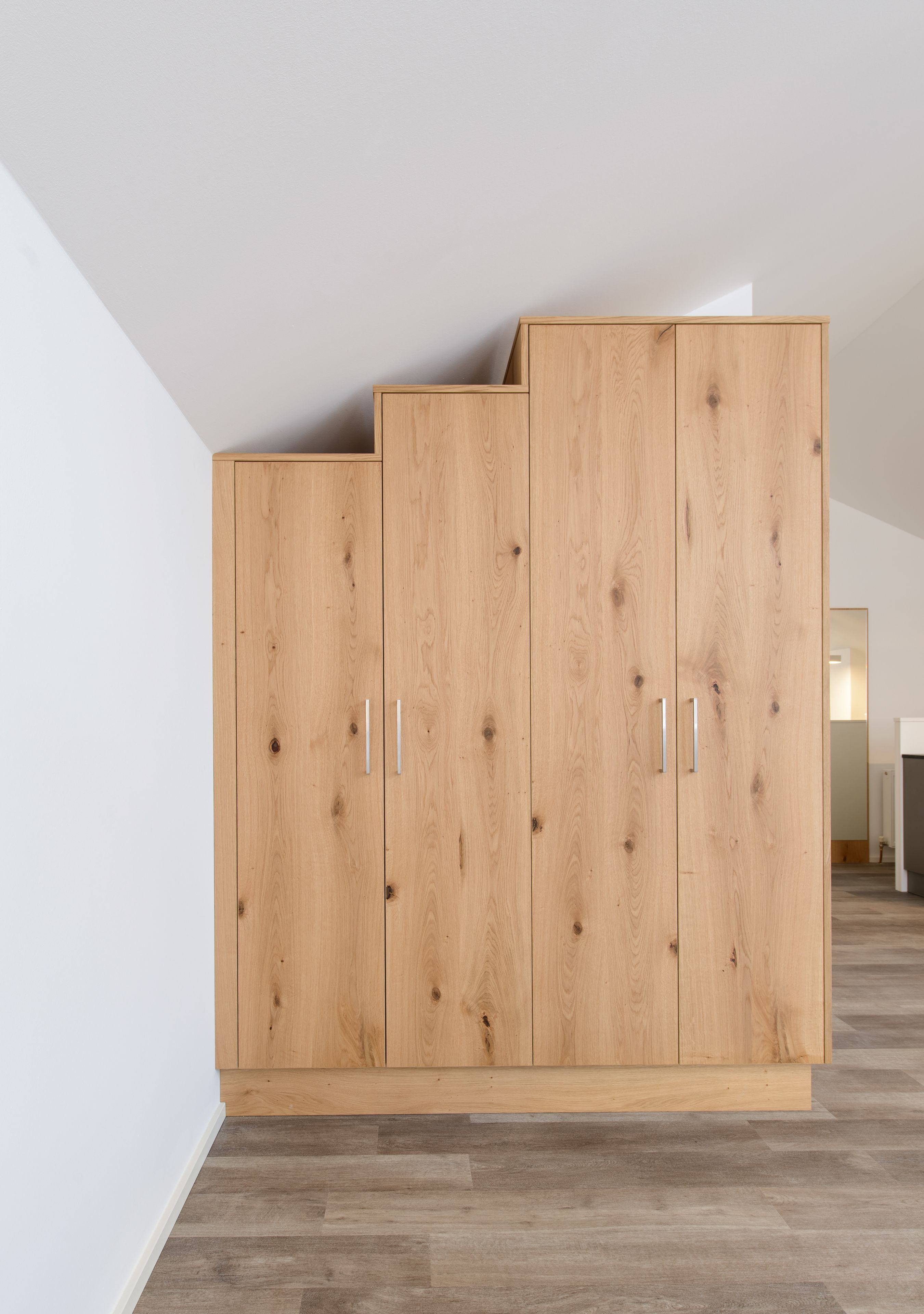 A wooden wardrobe with two doors and a shelf, located in a room with a sloped ceiling and wooden flooring.