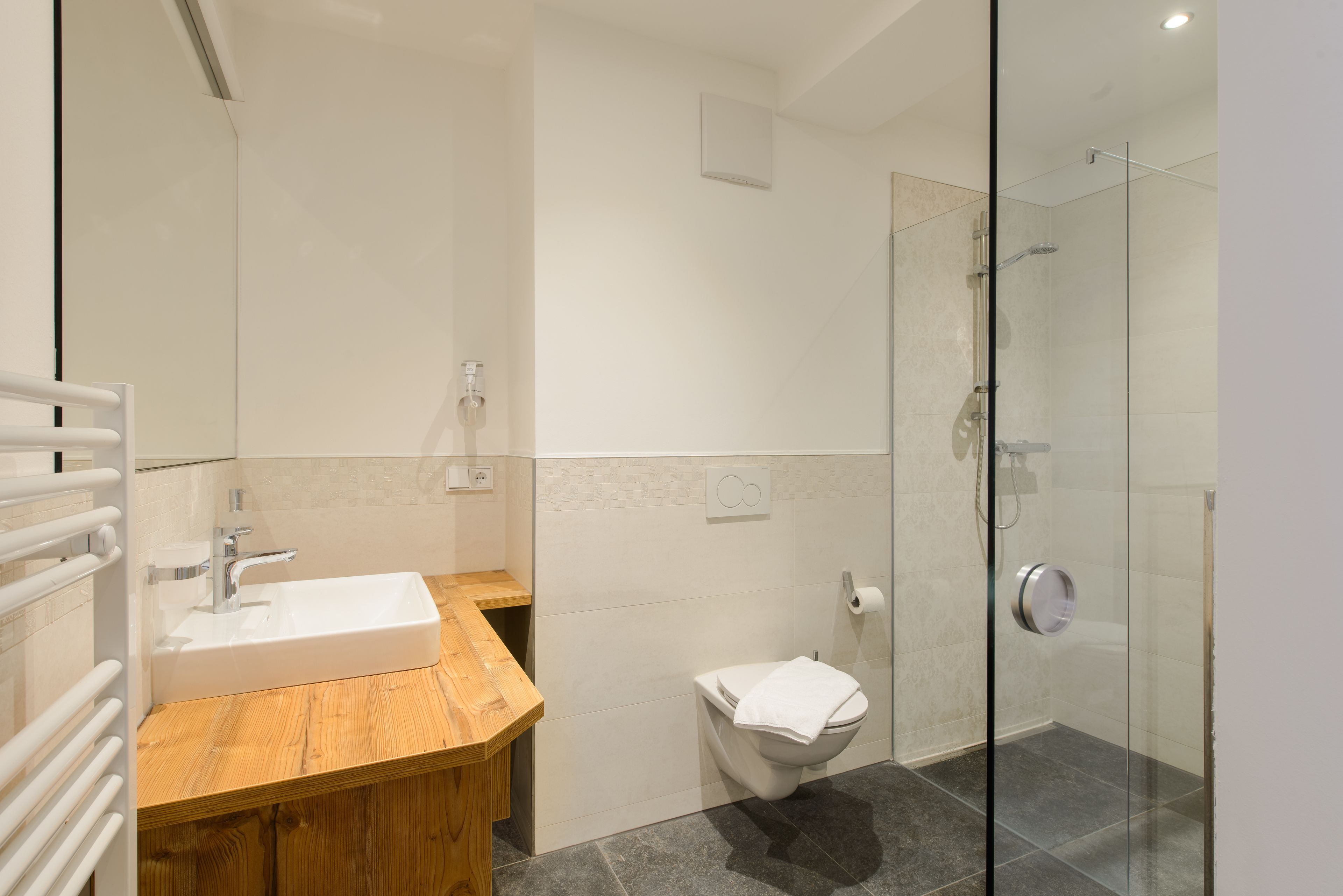 Ein modernes Badezimmer mit Waschtisch aus Holz, einer weißen Spüle, einer Toilette und einer gläsernen Duschkabine.