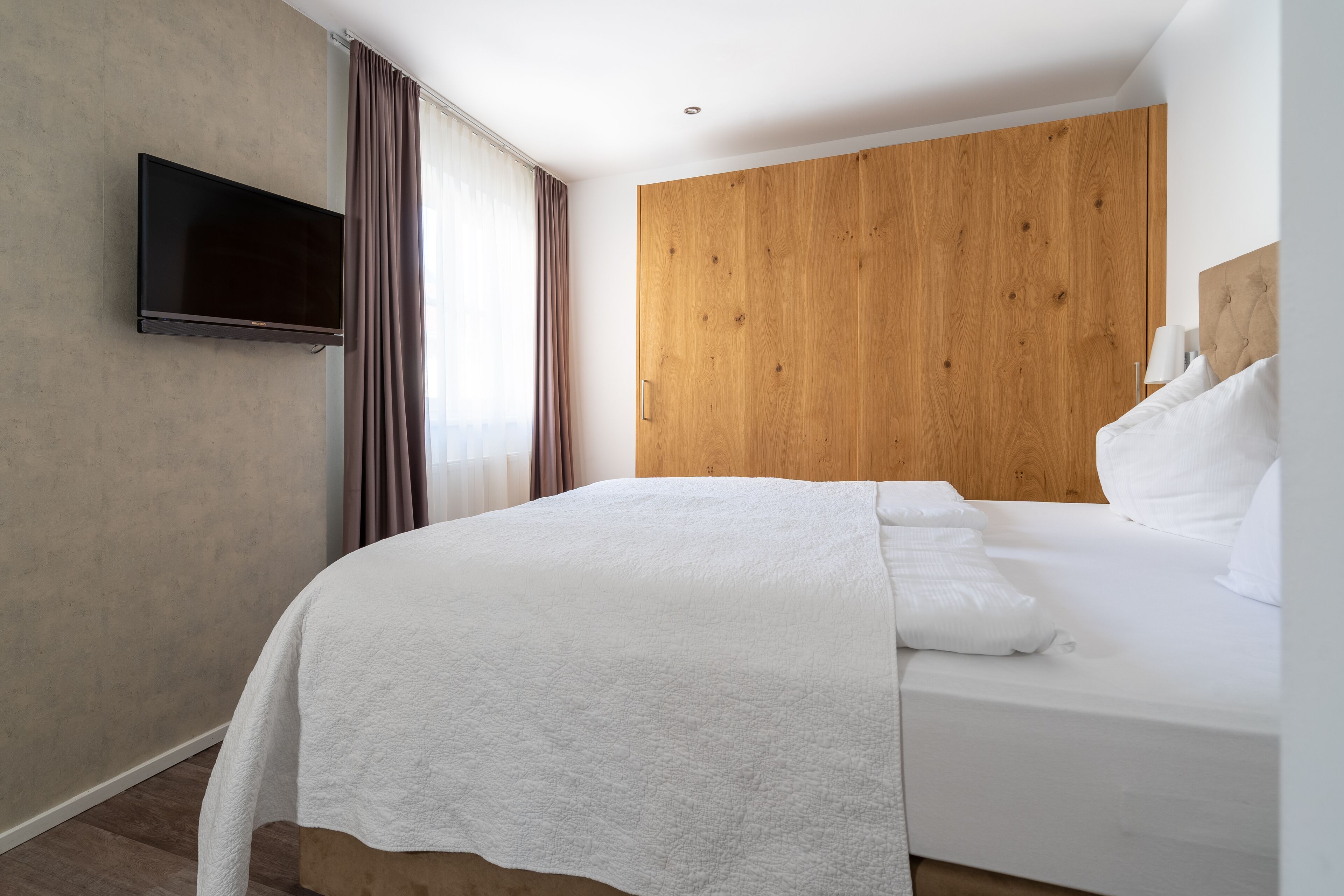 Une chambre d’hôtel moderne dotée d’un grand lit, d’un téléviseur à écran plat fixé au mur et d’une tête de lit en bois.