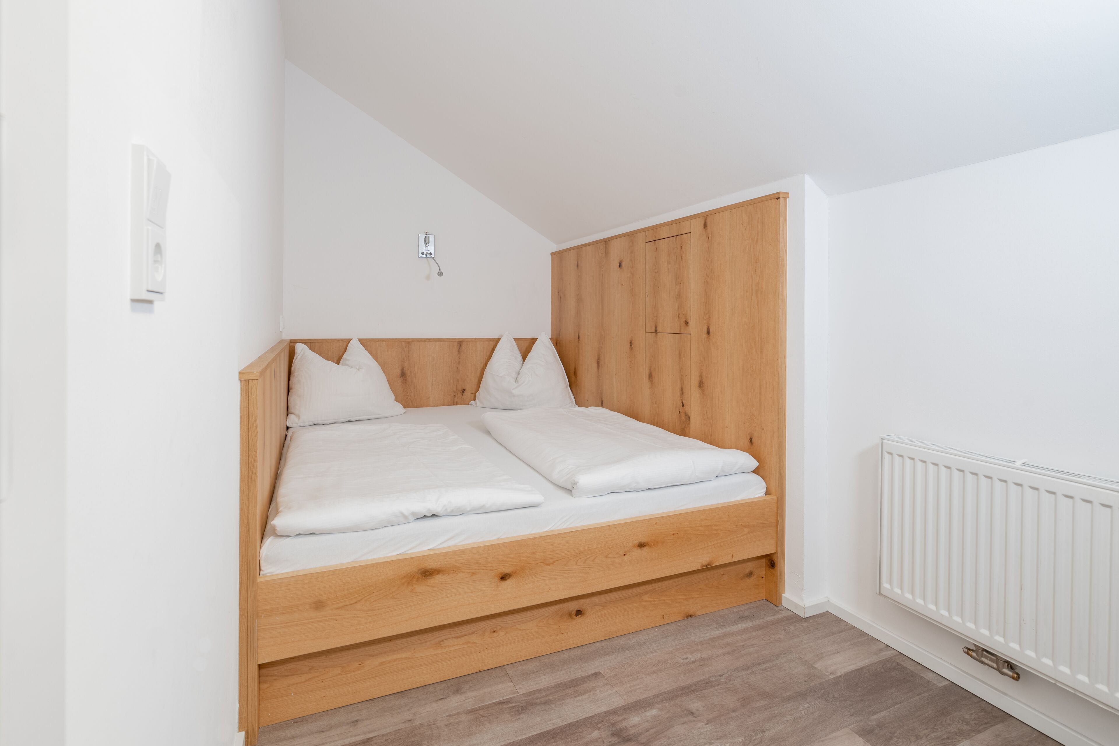 A bedroom with a wooden bed frame, white bedding, and a white radiator.