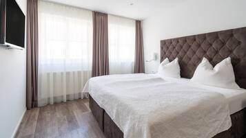 A modern hotel room with a large bed, a flat-screen TV mounted on the wall, and a large window with curtains.
