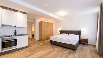 Een moderne slaapkamer met een groot bed, een houten garderobe, een kitchenette en een badkamer die door een open deur zichtbaar is.