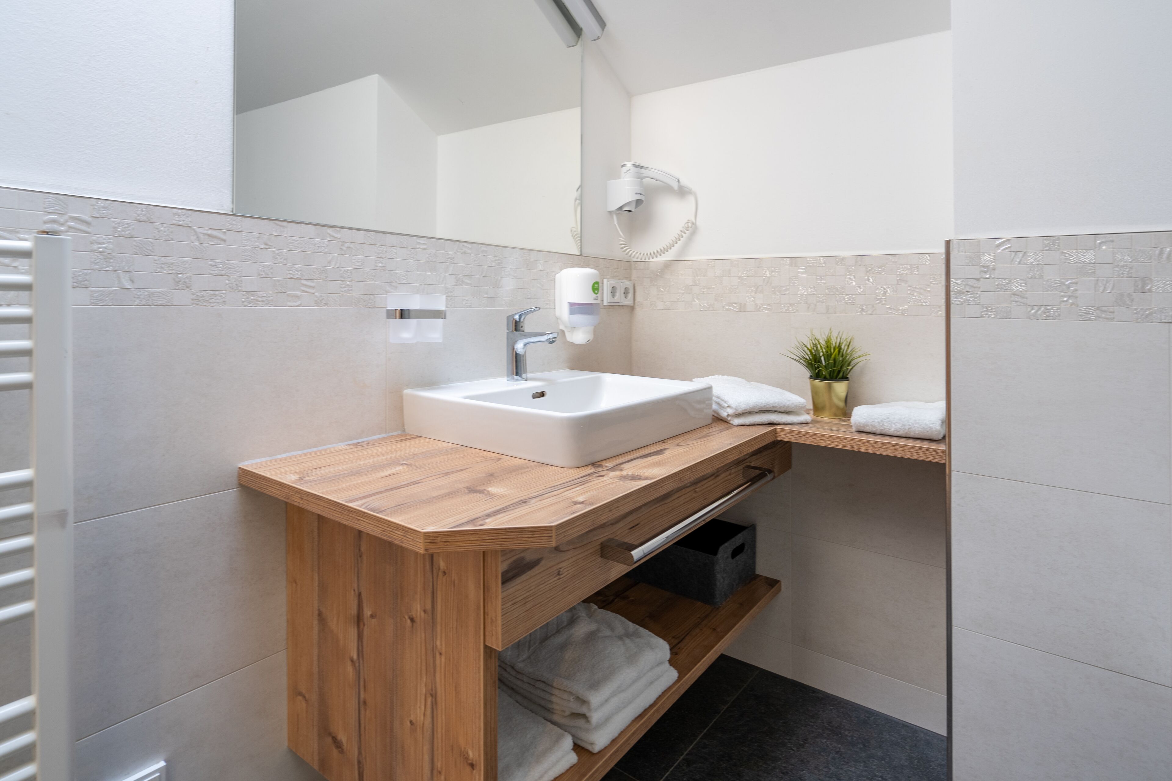Un baño moderno con tocador de madera, lavamanos blanco y espejo.