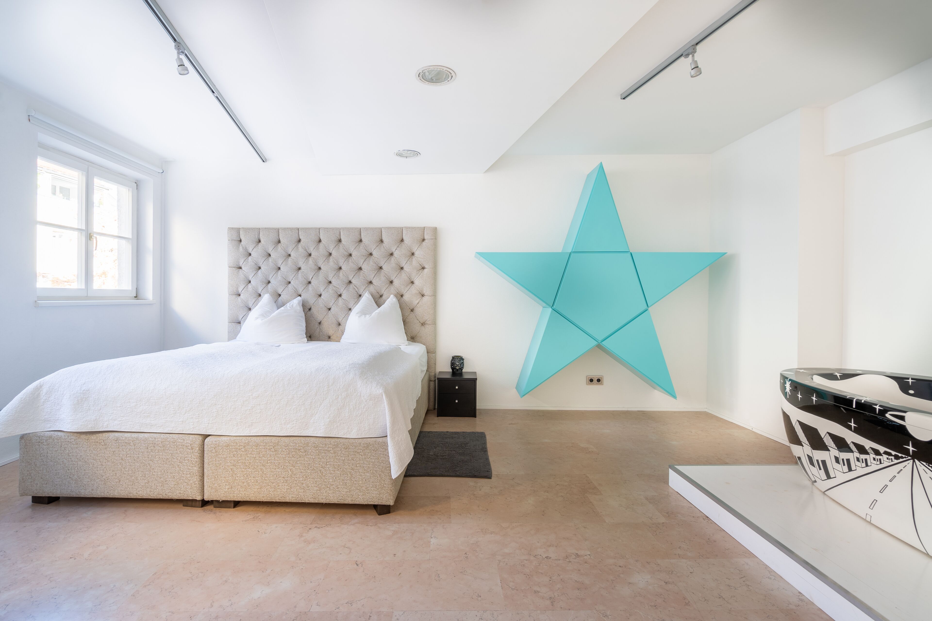 A modern bedroom with a large bed, a star-shaped wall decoration, and a boat-shaped artwork on the wall.