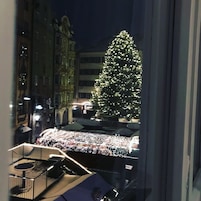A view of a Christmas tree decorated with lights, a balcony with a table and chairs, and a building with classical architecture in the background.