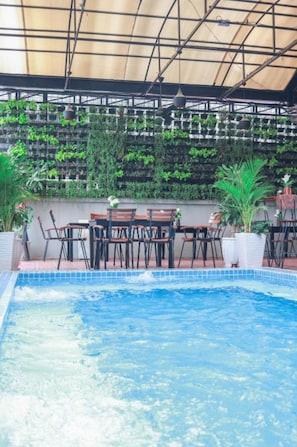 A pool area with a table and chairs, surrounded by lush greenery and a tiled floor.