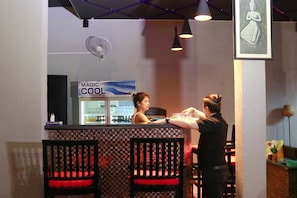 A bar area with a counter, chairs with red cushions, a fan, and a sign that reads "MAGIC COOL".