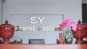 A reception desk with a sign reading "S.Y Guest House" and decorative items including two large red urns and a vase with pink flowers. - SY Guesthouse (Phnom Penh)