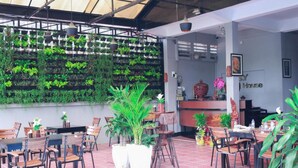 An indoor dining area with tables and chairs, a reception desk, and a wall of greenery. - SY Guesthouse (Phnom Penh)