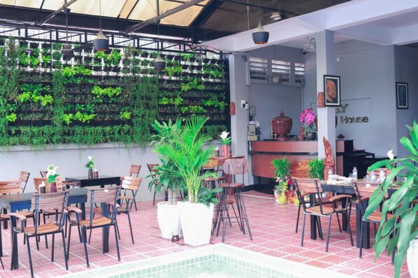 An indoor dining area with tables and chairs, a reception desk, and a wall of greenery.