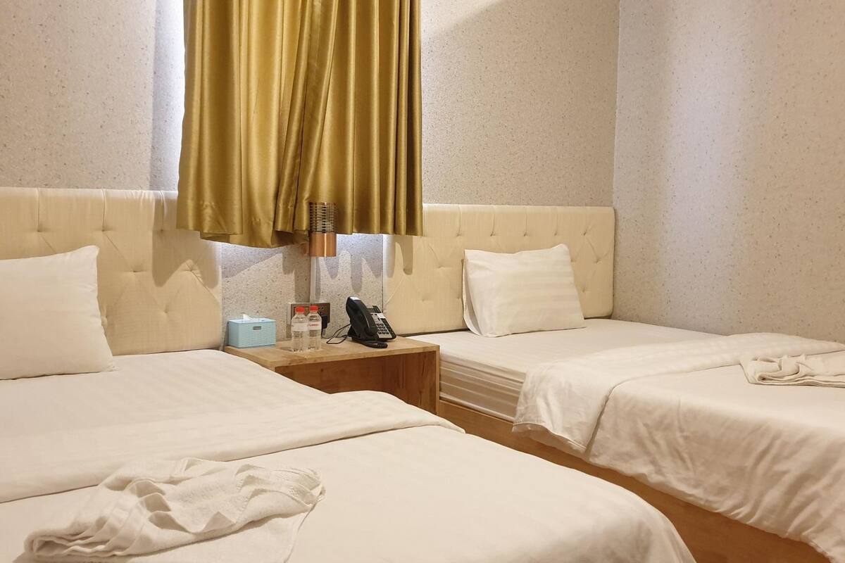 A hotel room with two beds, a bedside table with a lamp, a telephone, and a small table with a tissue box and water bottles.