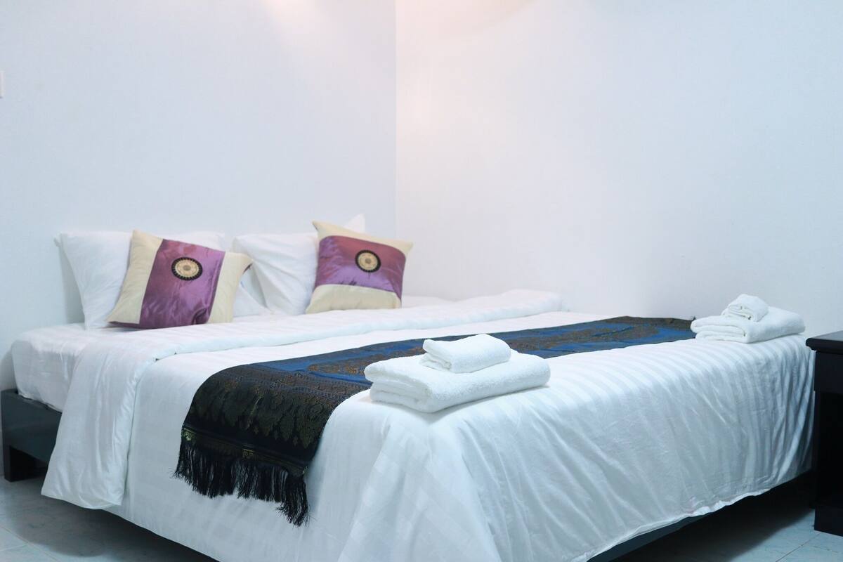 A neatly made bed with white linens, two pillows with a circular design, and a folded towel on the side.