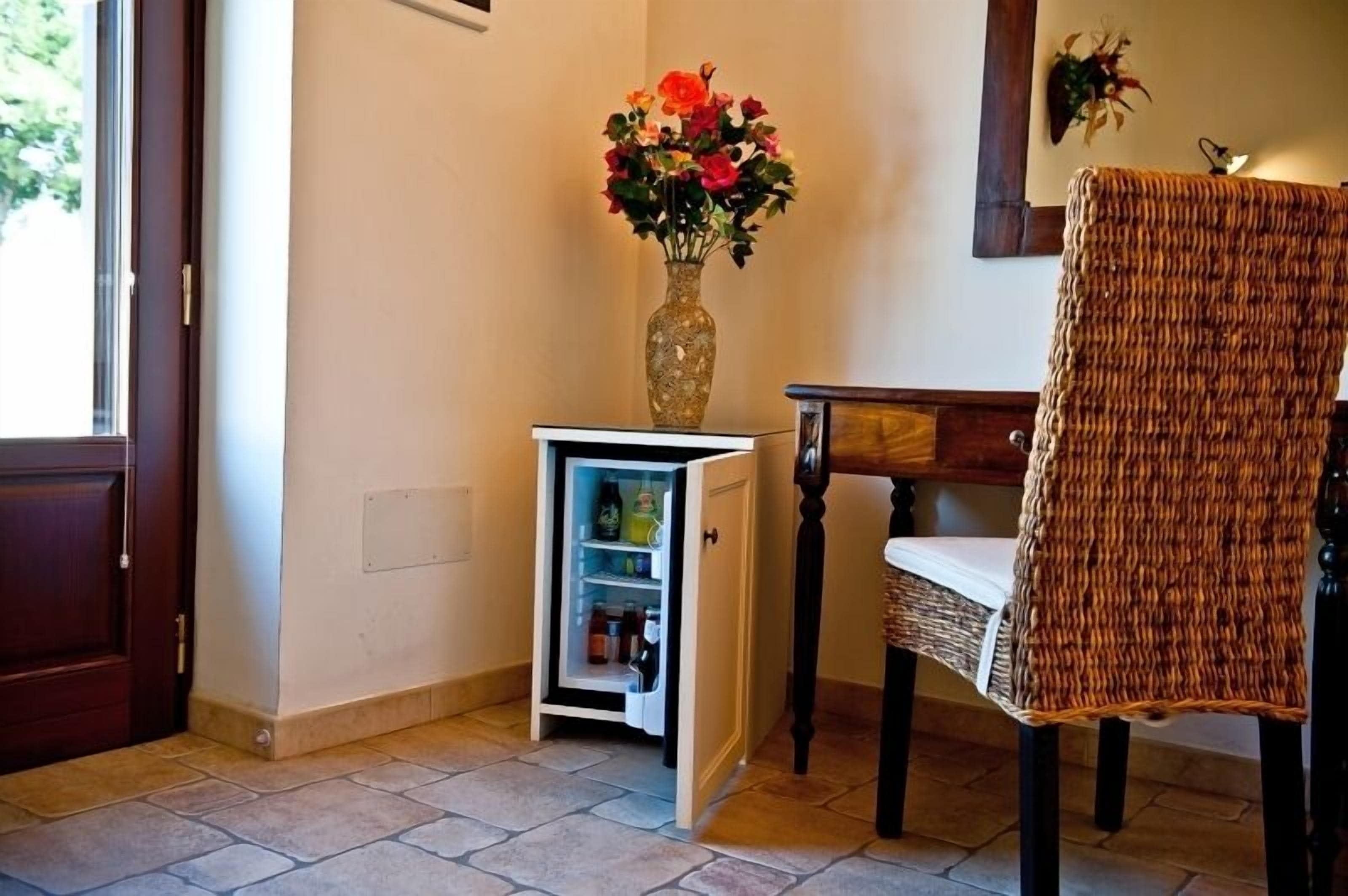 Cocina pequeña con refrigerador integrado, una silla de mimbre y un florero sobre una mesita.