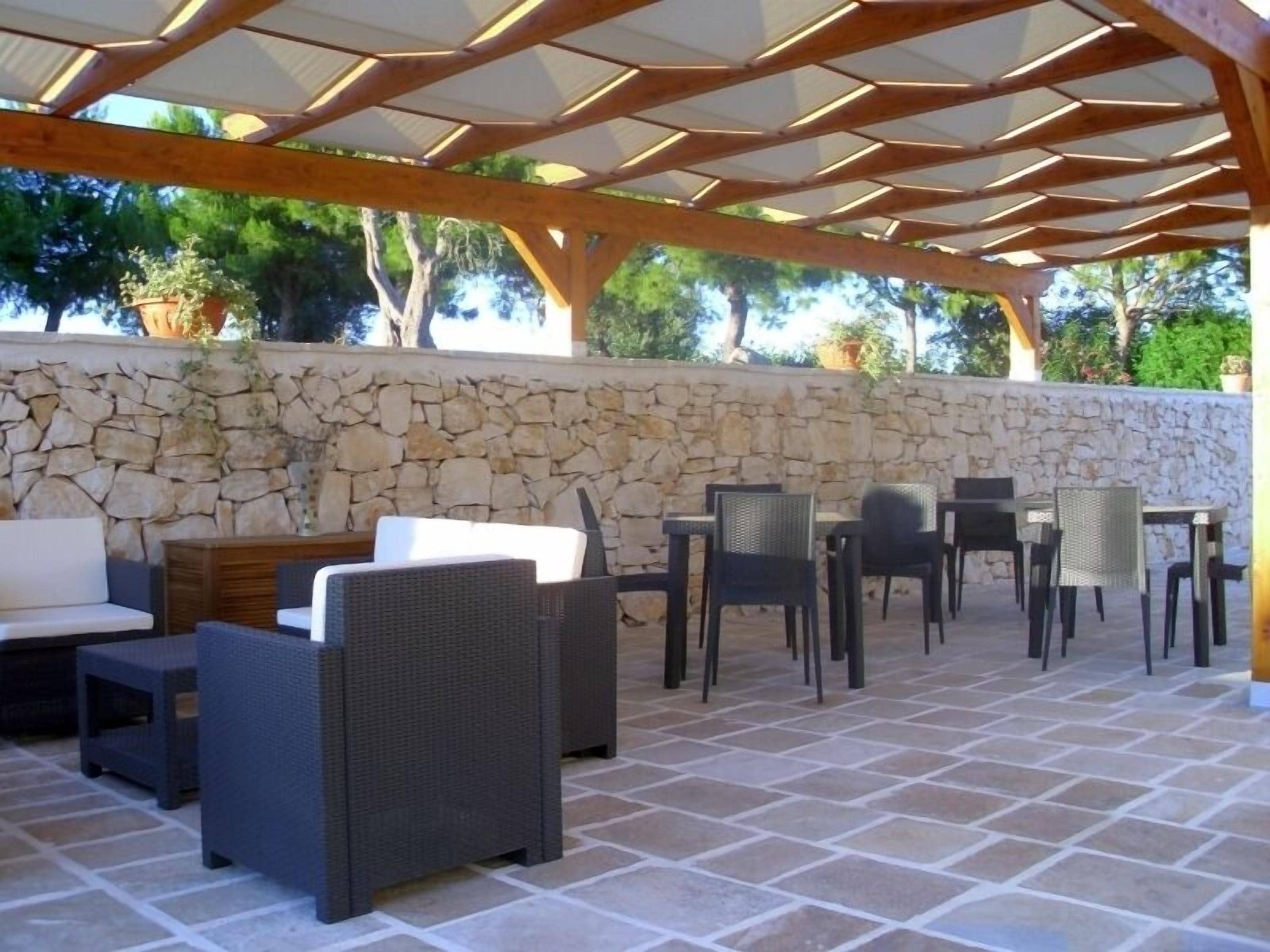 Een terras buiten met stenen muren, rieten meubels en een houten pergola.