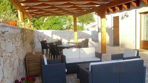 An outdoor patio area with a stone wall, wicker furniture, and a wooden pergola.