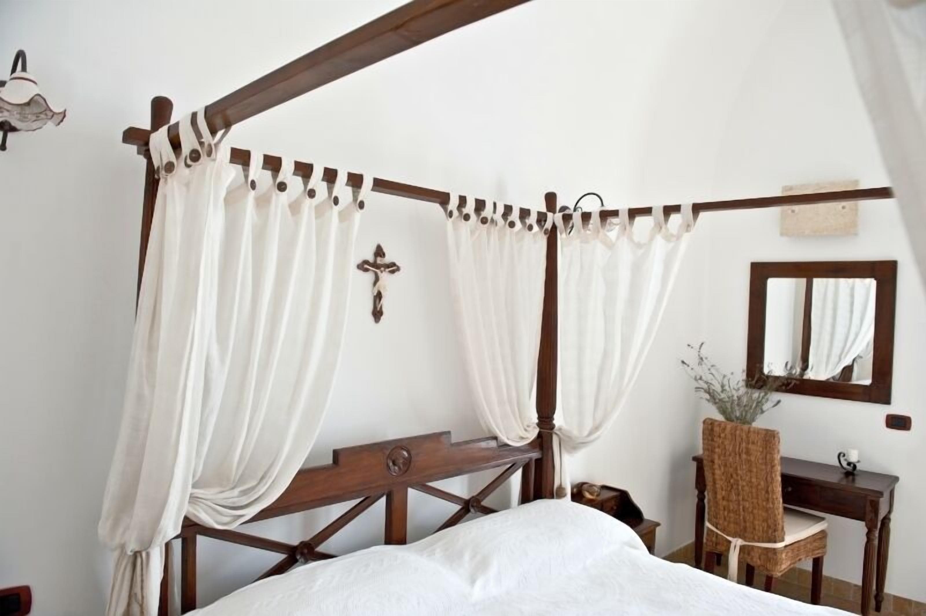 Camera da letto con letto a baldacchino, mobili in legno, uno specchio e una croce appesa al muro.