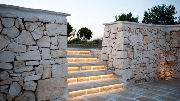 A stone staircase leading up to a building with a stone wall on one side.