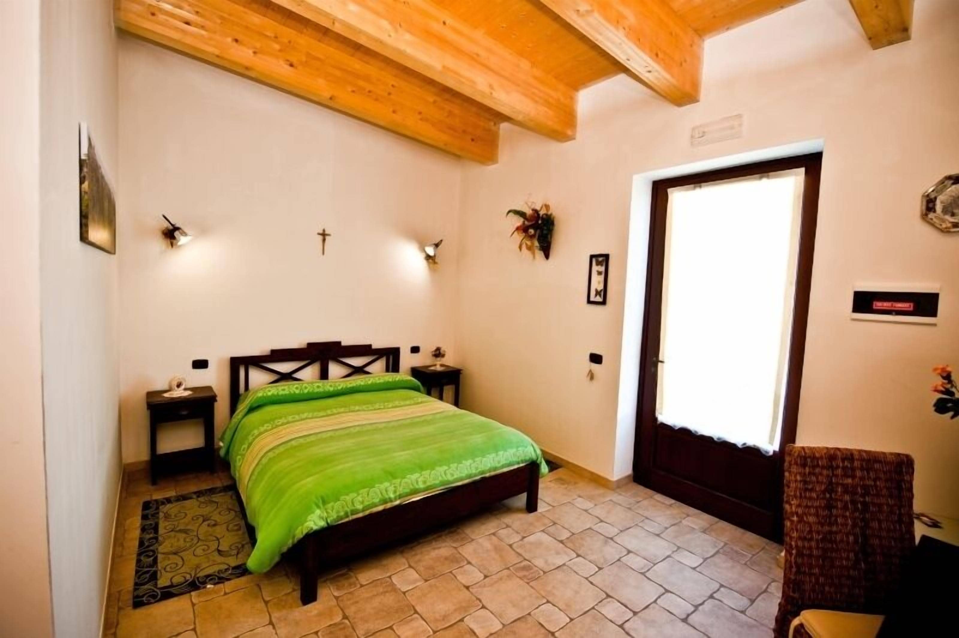 Un dormitorio con una cama, una mesita de noche, techo de madera, una puerta y una pequeña silla.
